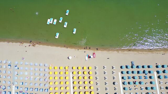 Top-down aerial drone view flying over rows of colorful beach umbrellas on sandy seashore in Cesenatico, Riviera Romagnola, Emilia-Romagna, Italy