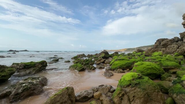 Strong low tide reveals the Atlantic Ocean floor with rocks covered in bright green moss in Cantabria, Spain.