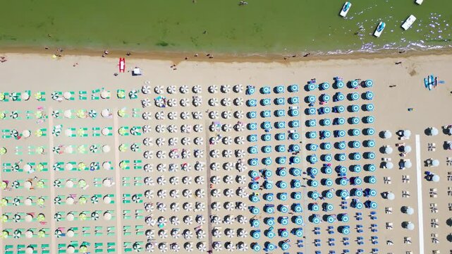 Top-down aerial drone view flying over rows of colorful beach umbrellas on sandy seashore in Cesenatico, Riviera Romagnola, Emilia-Romagna, Italy