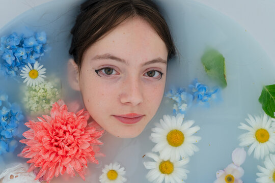 Young woman relaxing in floral milk bath with closed eyes and serene expression, with woman, young, portrait, relaxation detail, showing spa, milk, bath, milkbath context