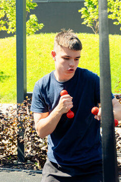 Young man working out with red dumbbells outdoors in a sunny park fitness area