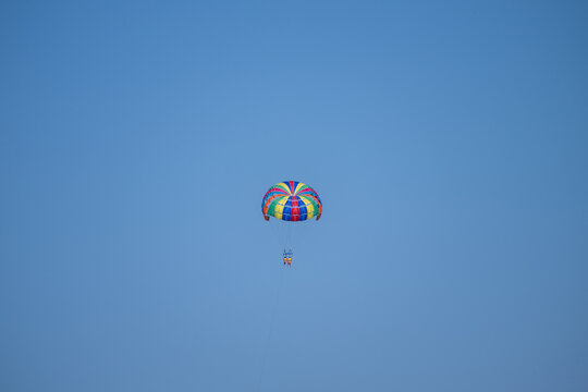 A colorful parasail carrying two people soars high in the clear blue sky.