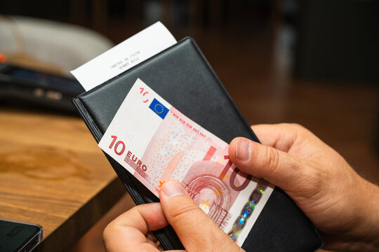 A person holds a black bill folder containing a ten-euro banknote and a guest receipt.