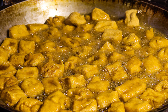 Scooping Golden Tahu Sumedang Tofu Cubes from Hot Oil Wok Using Metal Strainer Skimmer