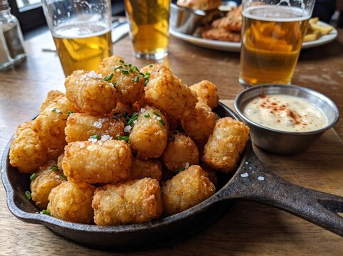 Crispy potato tater tots in a cast iron skillet with beer and dip