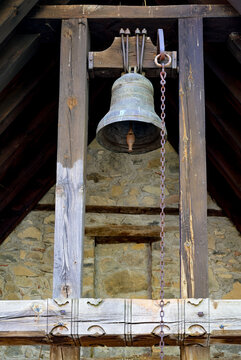 Old bronze bell hanging in a rustic wooden structure against a stone wall