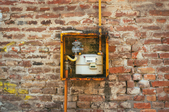 Utility gas counter enclosed in a metal box on a weathered brick building facade. Concept of residential energy supply, natural gas infrastructure, utility measurement, and urban property maintenance.