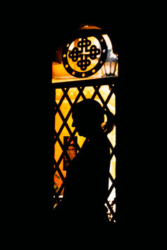 Silhouette of a praying woman against a glowing chapel window. Concept of Christian faith, personal devotion, spiritual peace, inner prayer, worship, and divine light.