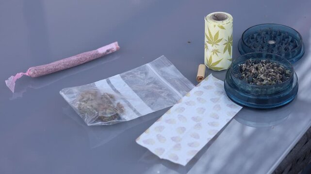 Smoking paraphernalia with cannabis buds, grinder, rolling papers, and a finished pink joint