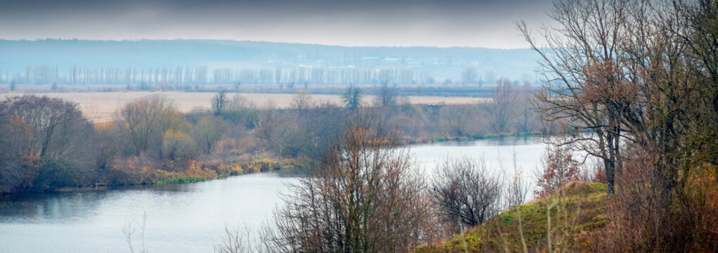 Autumn landscape with river among bare trees and fields
