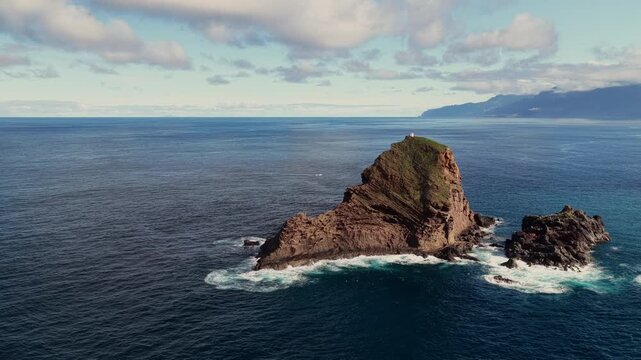 Drone aerial of Farol do Ilh&eacute;u Mole in Porto Moniz, Madeira, Portugal, featuring the historic lighthouse on a rocky islet surrounded by the Atlantic Ocean.
