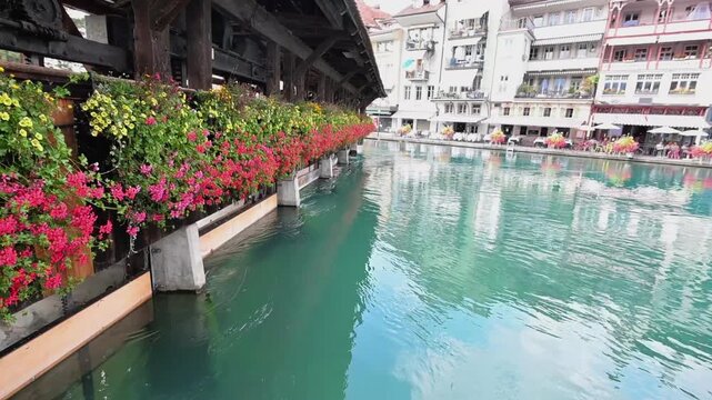 Turquoise Aare River water reflecting traditional riverside buildings and colorful flower boxes in central Thun, Switzerland.