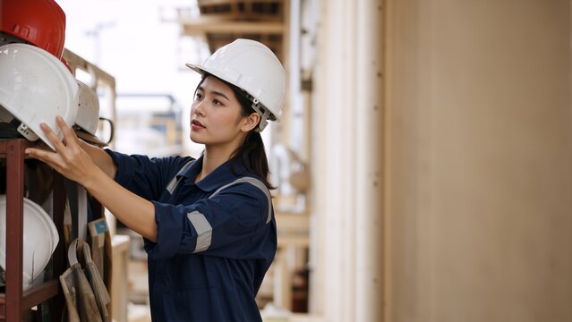 Young Asian female industrial worker taking hard hat from storage rack. Woman in blue uniform preparing for work. Copy space