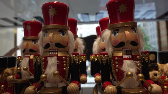 Wooden nutcracker soldiers stand in row, polished and ready. Red hats gleam under bright shop lights. Each figure holds drum, wears gold trim. They look cheerful, welcoming holiday shoppers.