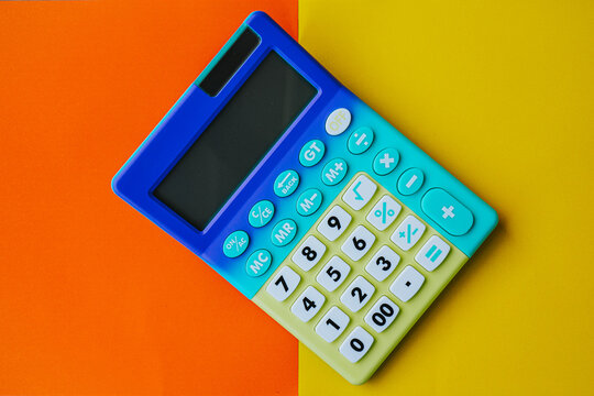 Colorful plastic calculator with blue and green buttons placed on a vibrant orange and yellow background, showcasing a modern design suitable for educational use