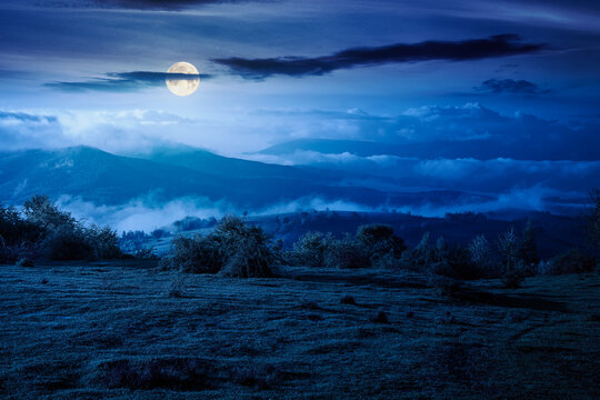 carpathian mountain landscape with fog at night. outdoor adventure image for stunning view of meadow. full moon over mountain field and rolling countryside valley. dark sky for mysterious fantasy