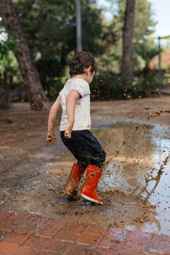 Toddler playing in mud puddle wearing red boots