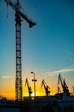 Shipyard cranes silhouetted against sunset sky. Industrial shipyard cranes stand in silhouette against a vivid blue and golden sunset sky above the waterfront.
