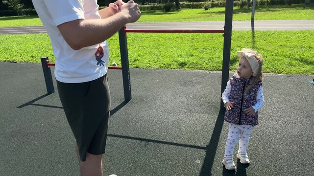 Father and daughter copy warm-up exercises at an outdoor workout area, playful family fitness, healthy parenting, active lifestyle, shared recreation.