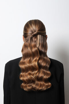 Back image of a long brown wavy hair of a woman, dressed in a black jacket.