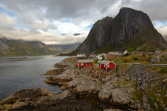 Malerische K&uuml;stenlandschaft mit traditionellen roten Fischerh&uuml;tten am Reinefjord und dem imposanten Berg Festhelltinden im Hintergrund, Hamn&oslash;y, Lofoten, Norwegen, Europa