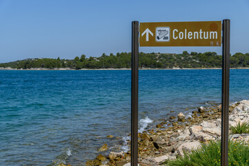 Brown tourist signpost marking the ancient Colentum archaeological site above the blue Adriatic, Murter, Croatia © Michal Plevko