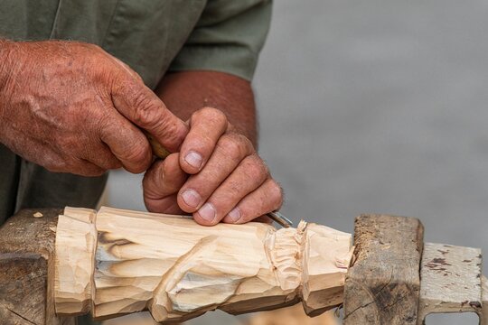 Craftsman hand-carving wooden figure with chisel on workbench