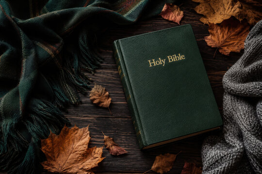 Closed Christian bible with green blanket and autumn leaves on a dark wood background