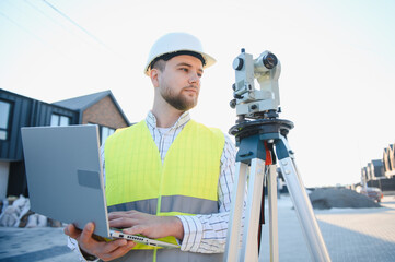 Land surveyor working with laptop and theodolite on construction site