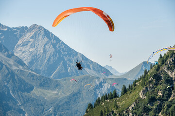 Paraglider flying with bright orange wing high above mountain valley in Chamonix French Alps during scenic summer day with extreme tandem flight adventure travel experience over alpine landscape © Soloviova Liudmyla