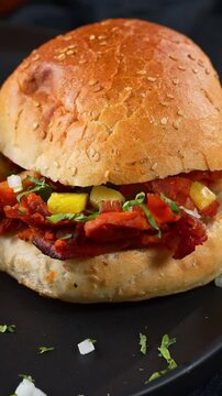 Close up of al pastor cemita sandwich with sesame seed bread served on dark plate
