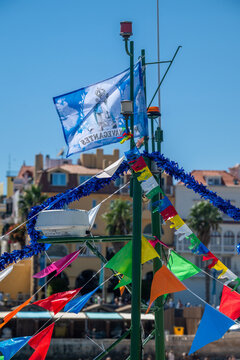 Cascais, Portugal - 30 August 2026: View of festive flags and decorations on a mast in Cascais, with historic buildings and palm trees in the background under a clear blue sky.