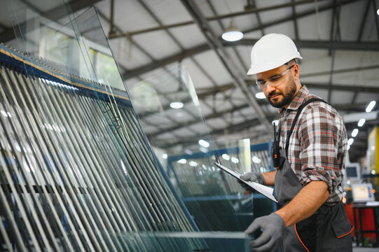 Worker inspecting glass panels in window manufacturing factory