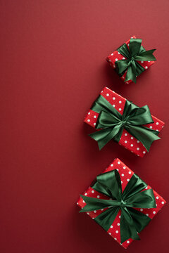 Red polka dot presents with green bows for Christmas and New Year holiday celebration ob vertical maroon background
