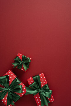 Merry Christmas and Happy New Year red wrapped gift with green bow and polka dot paper on vertical burgundy backdrop with a lot of space for text