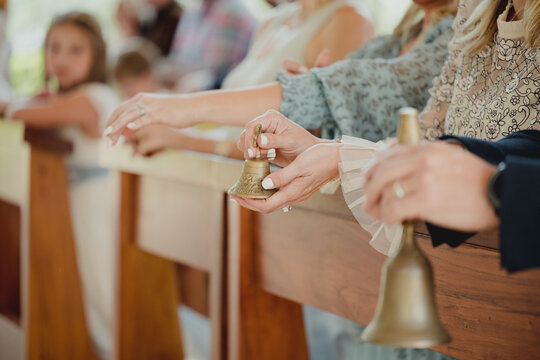 Close-up of hands holding small golden handbells during an elegant wedding or ceremonial celebration.
