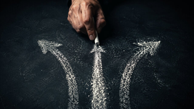 Hand drawing three different directional paths with chalk on a dark surface, symbolizing choices, decisions, options, future planning, strategy, dilemma, and pathfinding   
