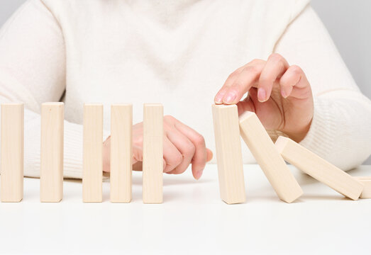 Woman's hand stopping falling wooden blocks, preventing the domino effect on a white background