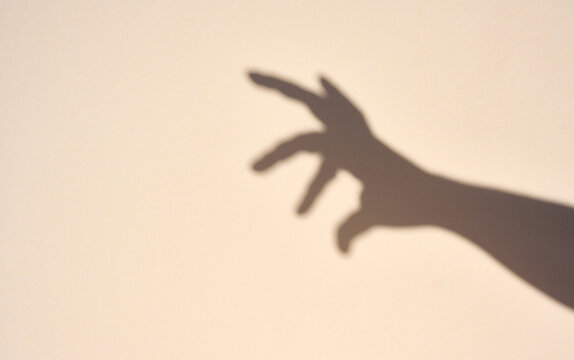 Sharp shadow of a hand on a light beige background.