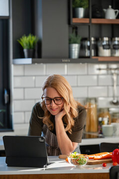 Woman using a digital tablet for healthy meal planning while preparing fresh vegetables and salad in her kitchen