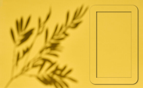 Empty rectangular frame and shadow of a plant branch on a yellow background for a mockup.