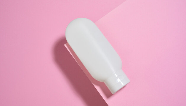 White plastic cosmetic tube on a pink background. Top view