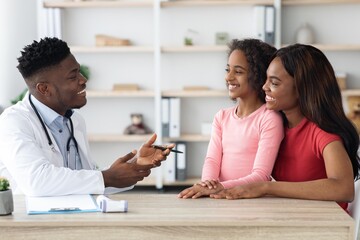 Fototapeta premium Smiling African American Doctor Engaging With Young Girl And Her Mother During Consultation At Clinic. Joyful Interaction Demonstrating Care, Support, And Professionalism In Healthcare Setting.