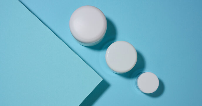 White cosmetic jars of various sizes on a blue geometric background.