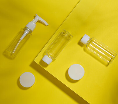 A set of transparent plastic bottles and jars with white lids on a yellow background
