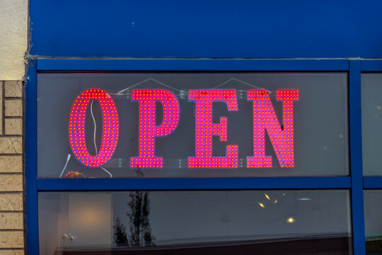 Close-up shot of a red LED open sign glowing brightly inside a storefront window on a blue facade.