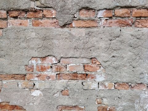 Weathered concrete wall with exposed old red bricks texture. Rough cement and brickwork background.
