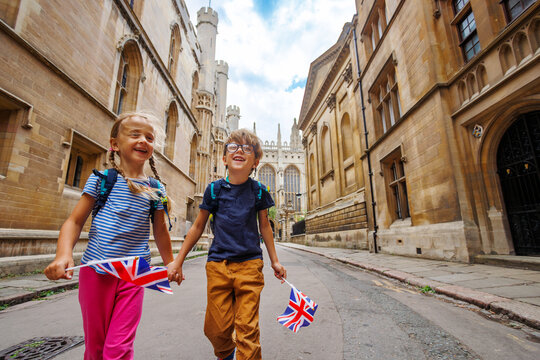 Laughing kids, boy, girl tourists walk Cambridge with flags, UK