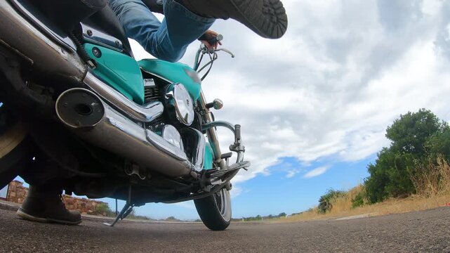 Slow motion low angle view of a biker getting off a custom motorcycle and lowering the kickstand, focusing on the rider foot and lower part of the motorcycle.