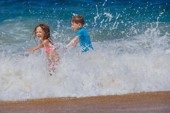 Kids have fun splashing through ocean waves along sandy beach